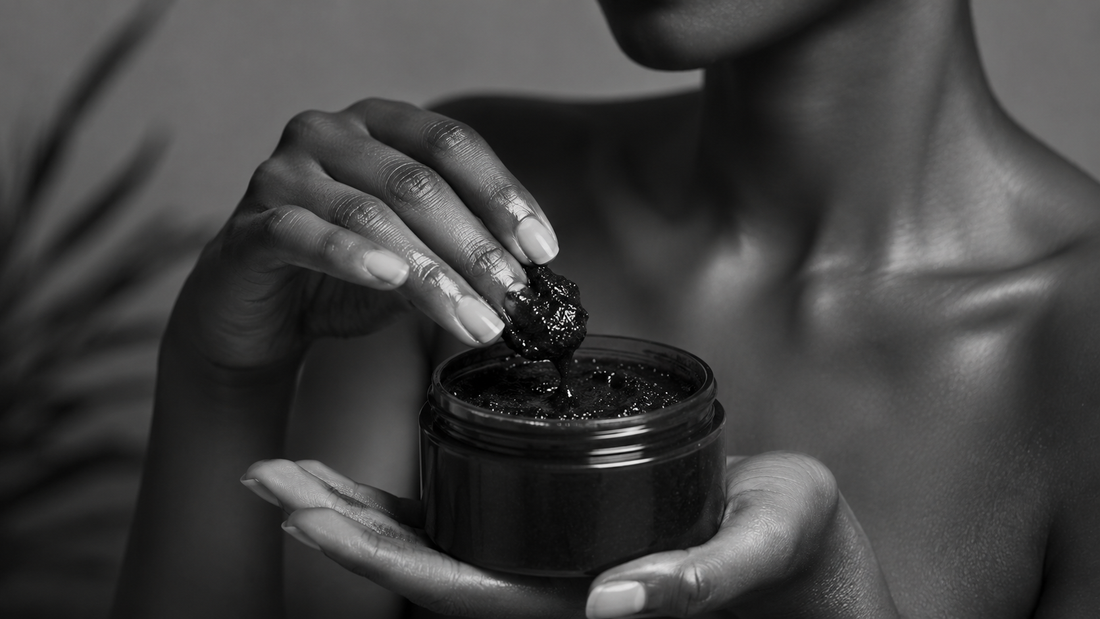 Black and white close-up of a woman holding a jar of African Black Soap paste and gently scooping the natural cleanser with her fingertips.